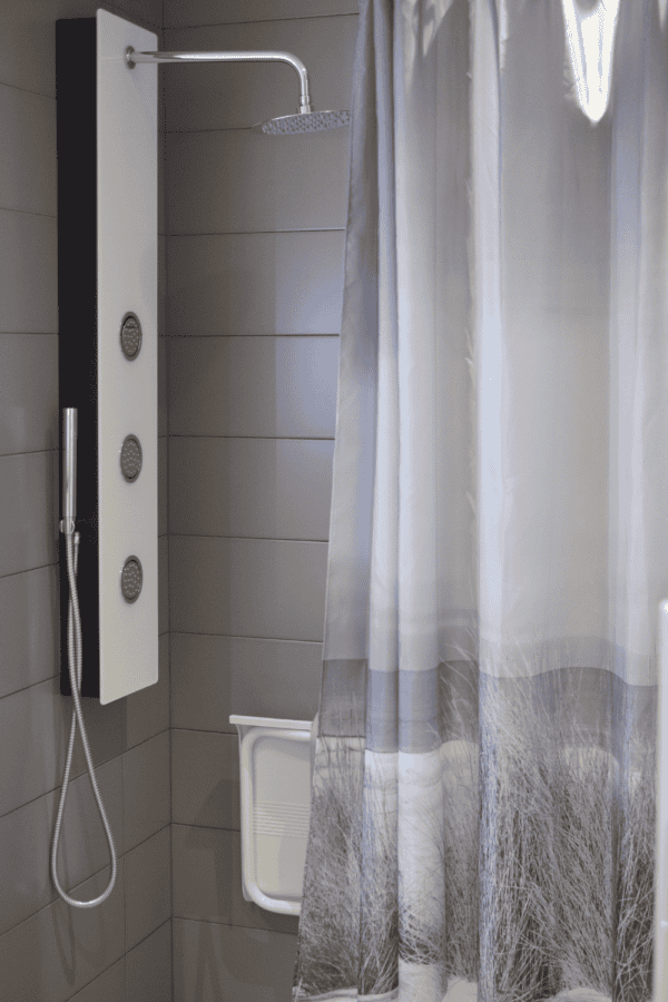 Modern bathroom with a gray and white shower curtain featuring a nature design, hanging beside a rainfall showerhead and a wall-mounted shower panel.