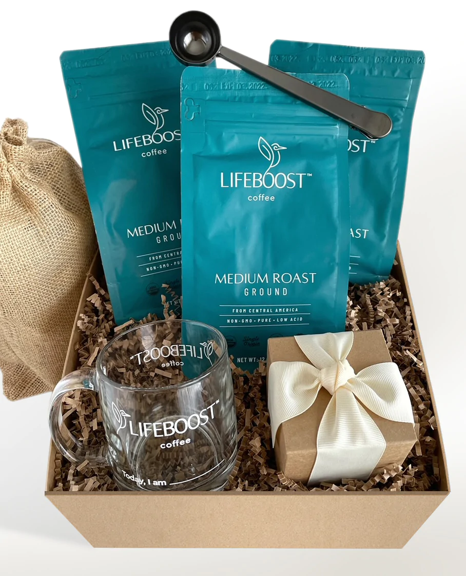 A brown cardboard box contains a Lifeboost Coffee gift set, including three bags of medium roast ground coffee, a glass mug, a coffee scoop, and a small gift-wrapped box.