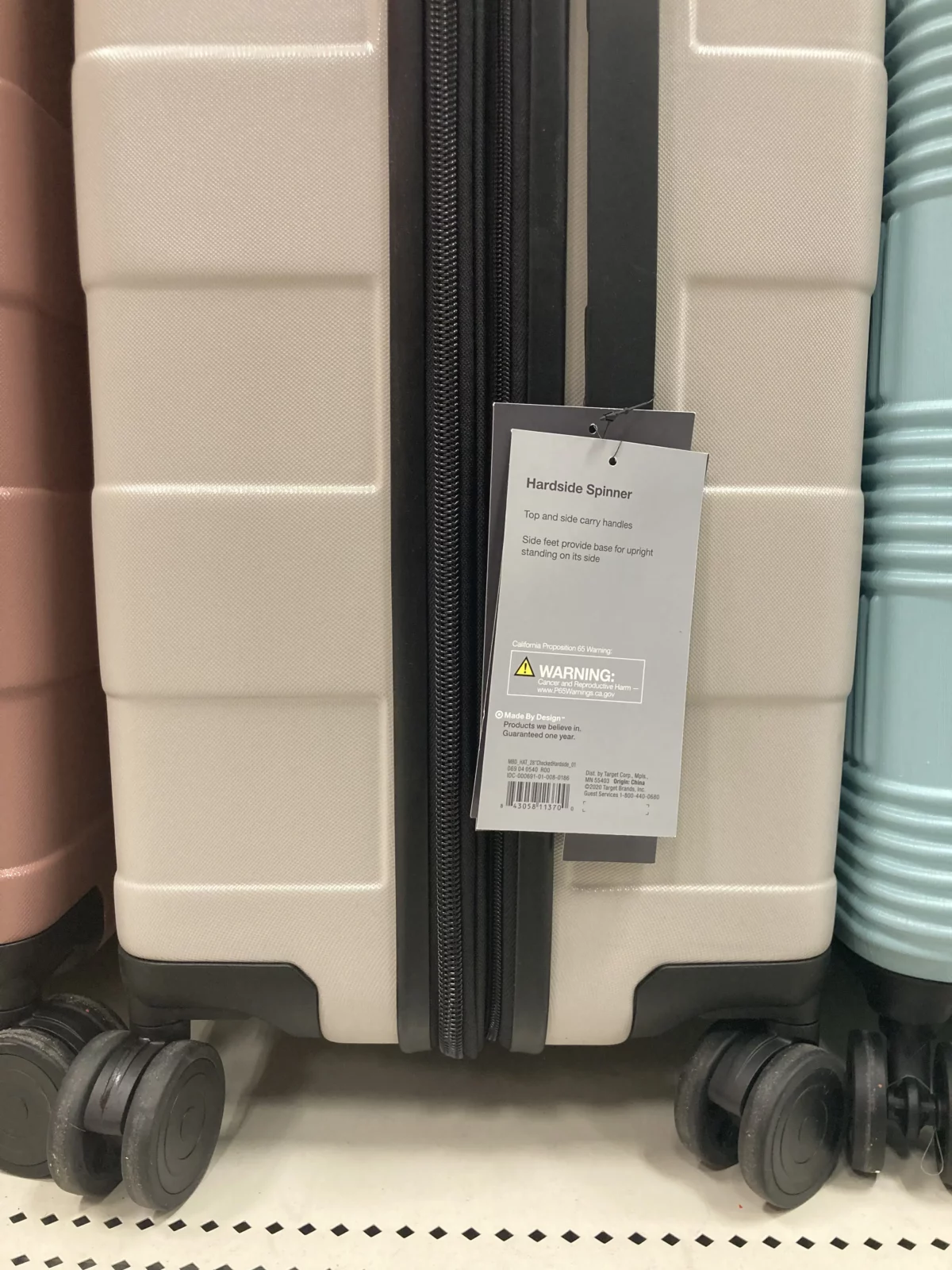 The photo shows a luggage with a product tag displaying a warning about California Proposition 65.