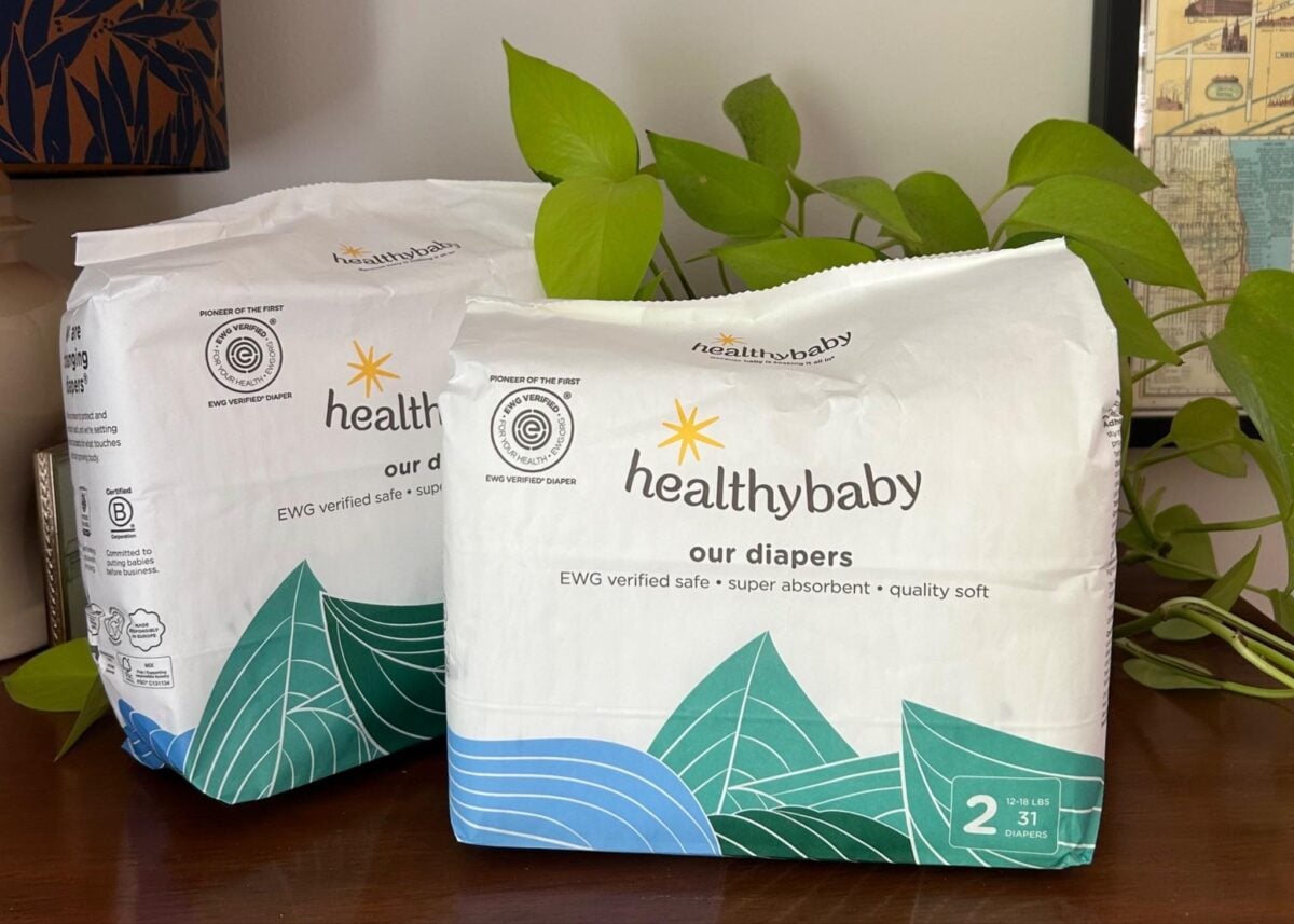 Two packages of healthybaby brand diapers labeled our diapers with green and blue leaf designs sit on a wooden surface near green leafy plants. Each pack contains 31 size 2 diapers for babies 12-18 lbs.