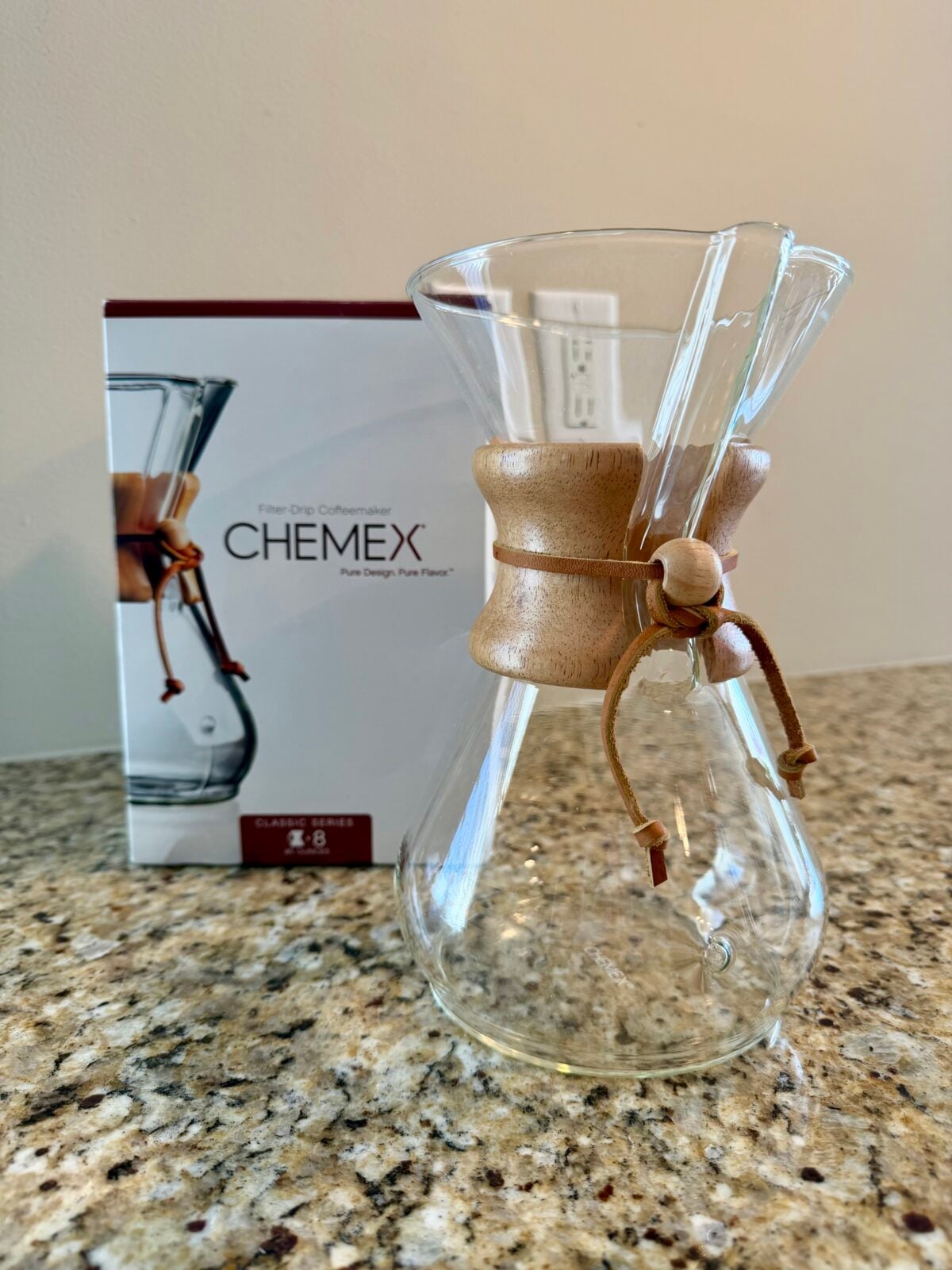 The photo shows a glass Chemex "Classic Series" pour-over coffee maker with its signature wood collar and leather tie, sitting on a granite countertop next to its original packaging.