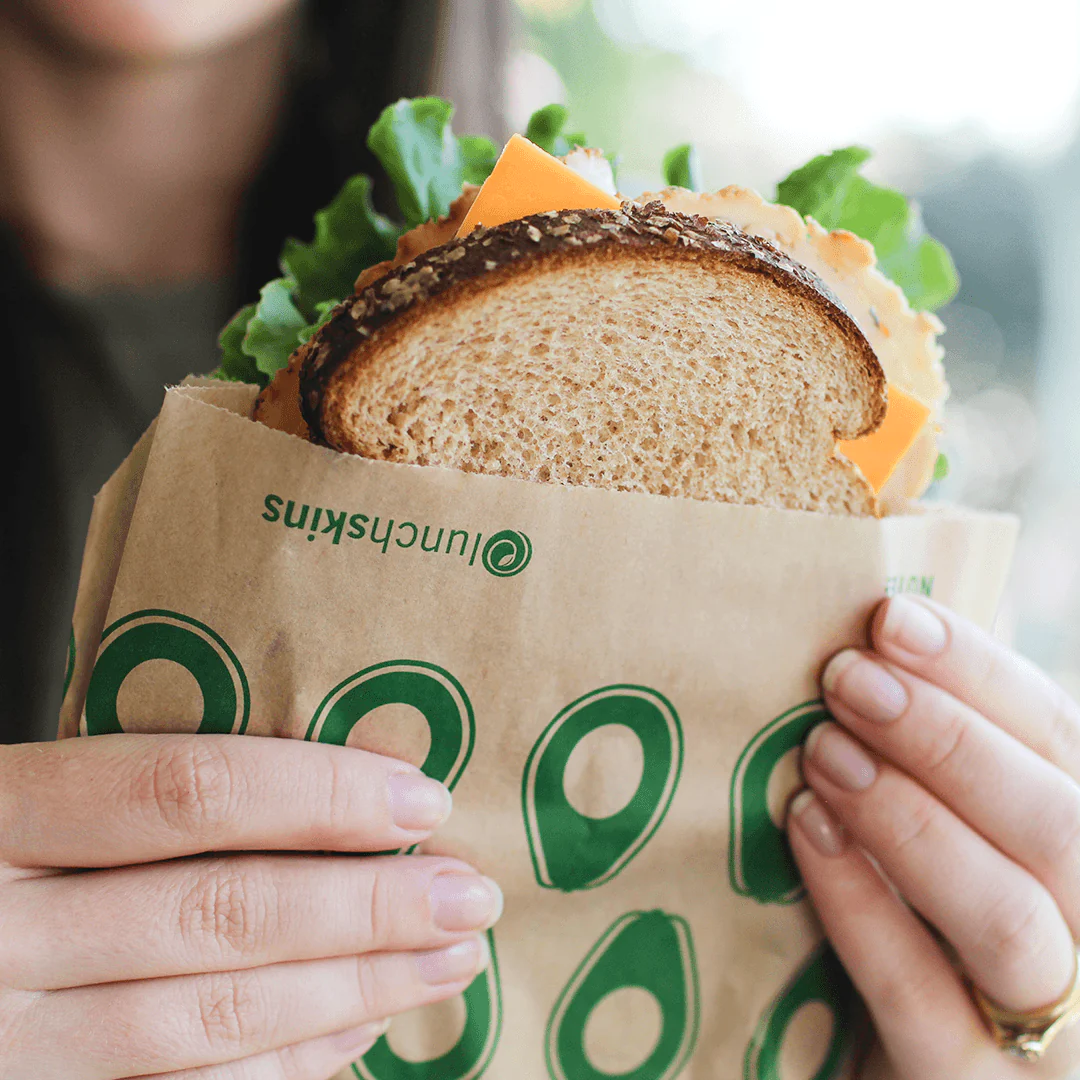 A woman holding up her sandwich inside the paper bag from Lunchskins.