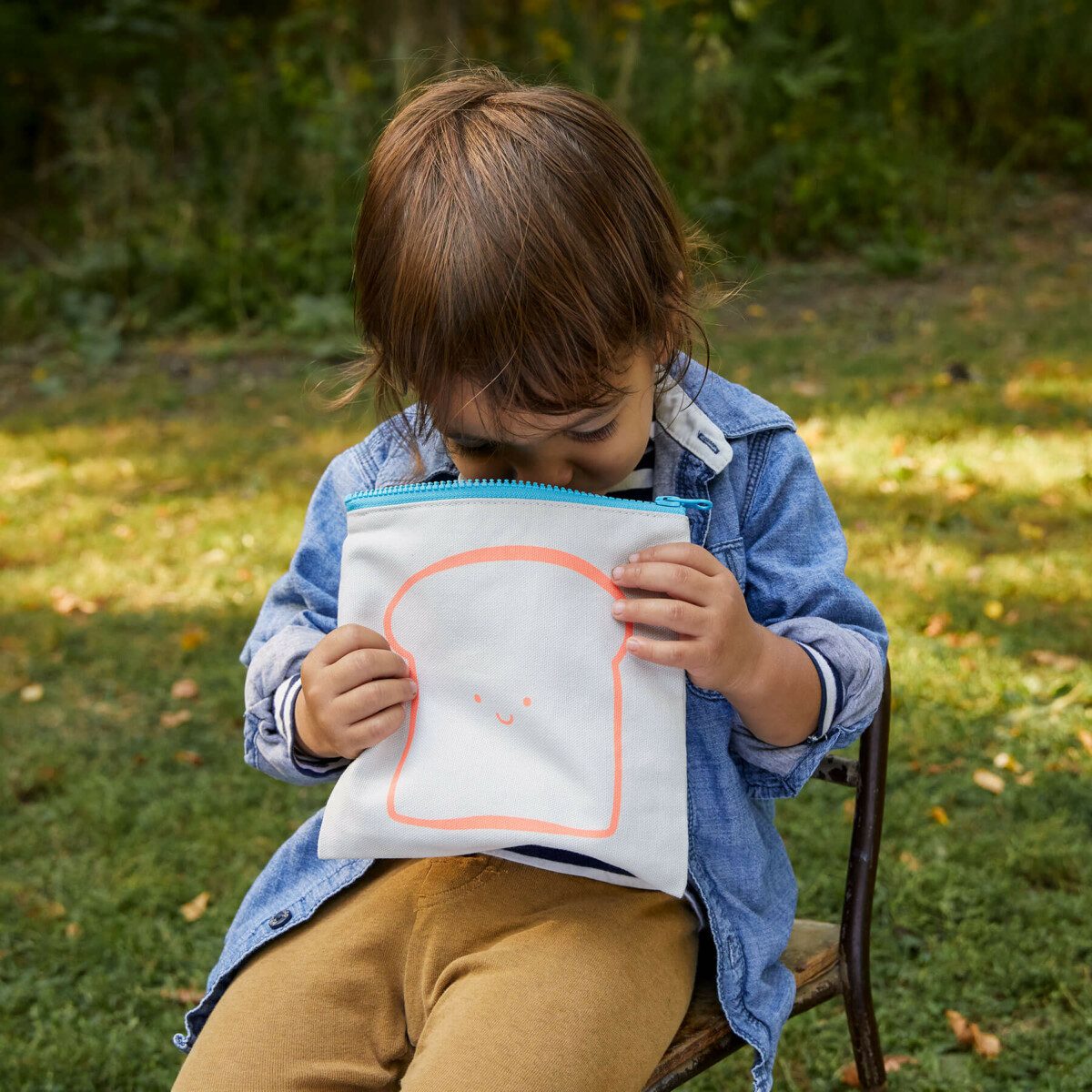 A boy sitting down, looking inside the organic cotton sandwich bag from Fluf.