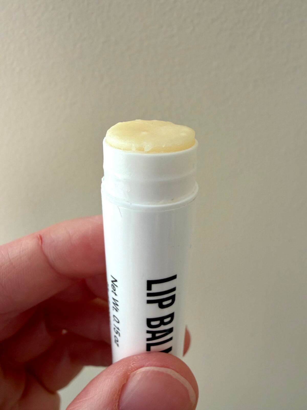 Hand holding Public Goods lip balm tube with cap removed, showing yellow balm at top