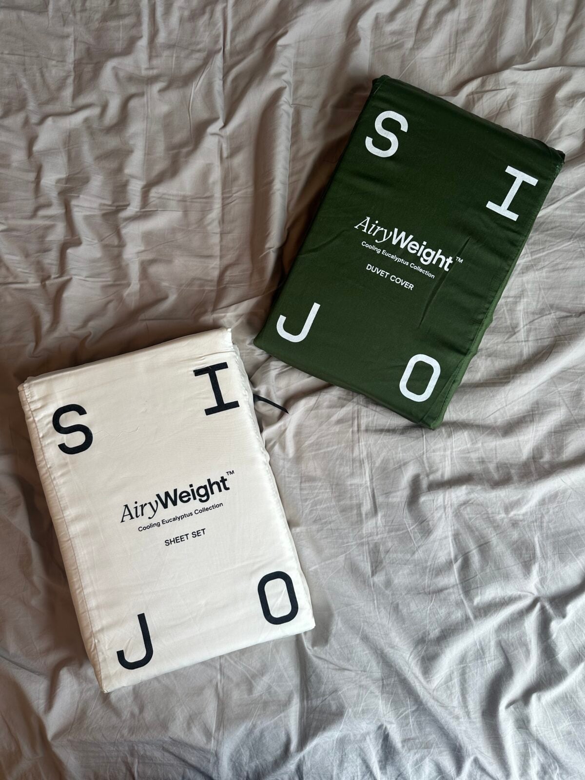 Two Sijo AiryWeight product packages - eucalyptus sheet set and duvet cover - on beige bedding