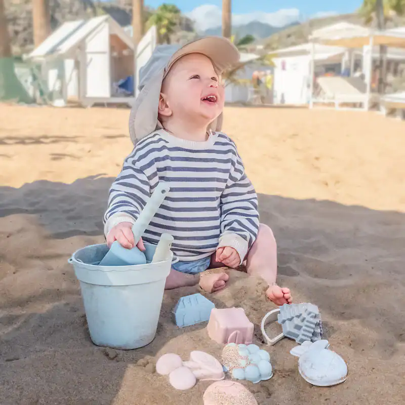 a baby sitting on the beach sand holding a silicone beach toys from Moonkie