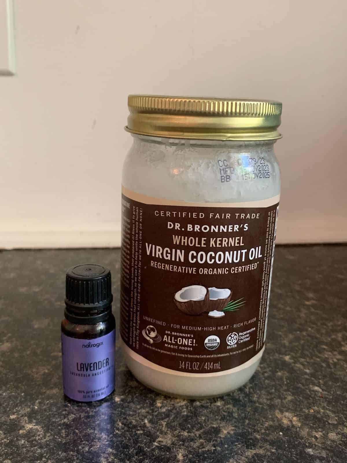 
A large jar of Dr. Bronner's Virgin Coconut Oil sits next to a small bottle of lavender essential oil on a dark countertop.