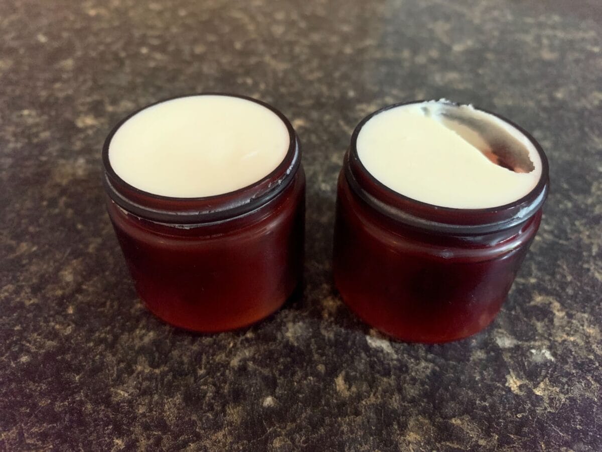 Two small, open, dark-colored jars of Whipped Cacao Body Lotion are shown on a dark countertop.