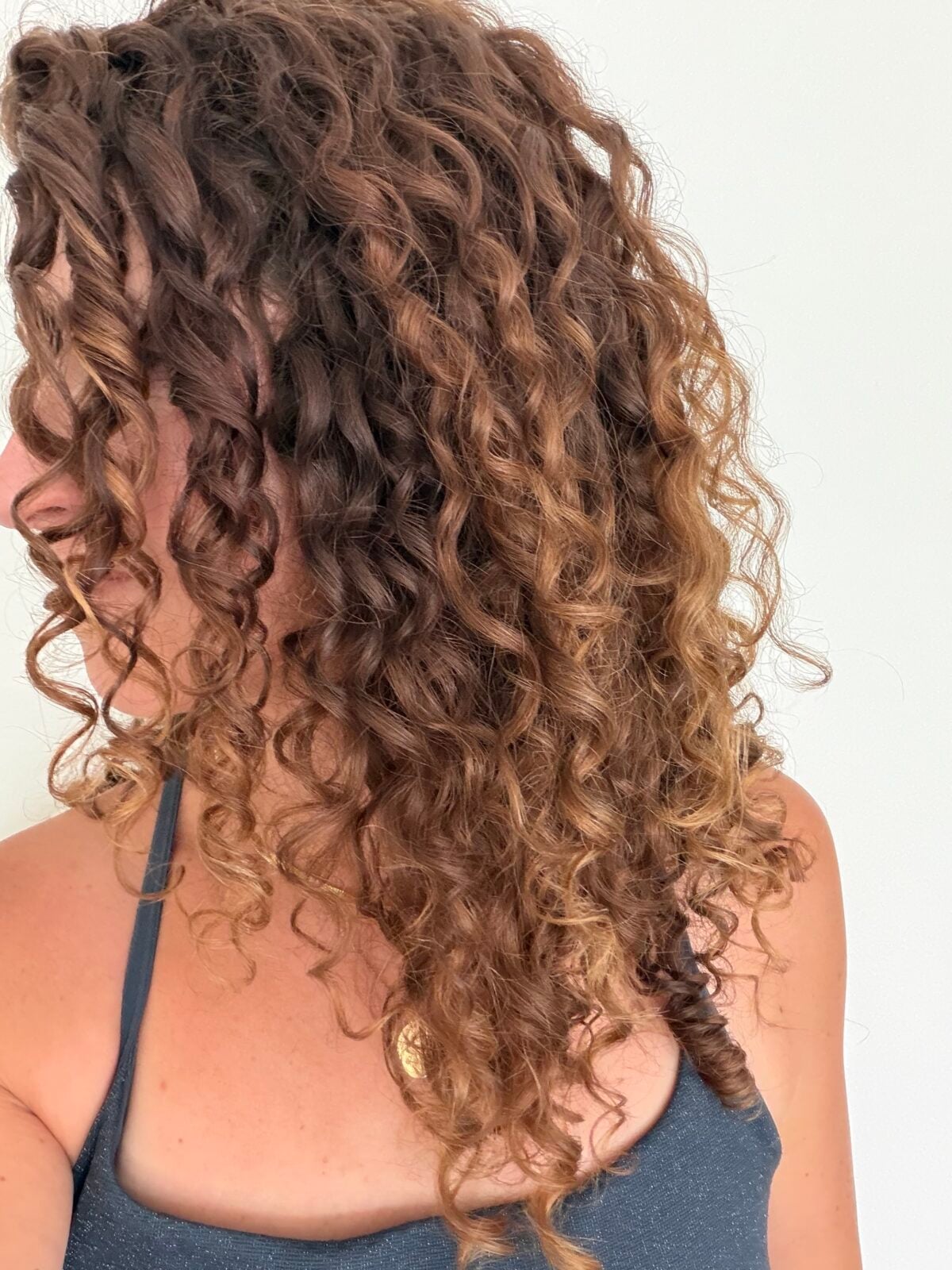 A profile view of a person with long, highlighted curly hair.