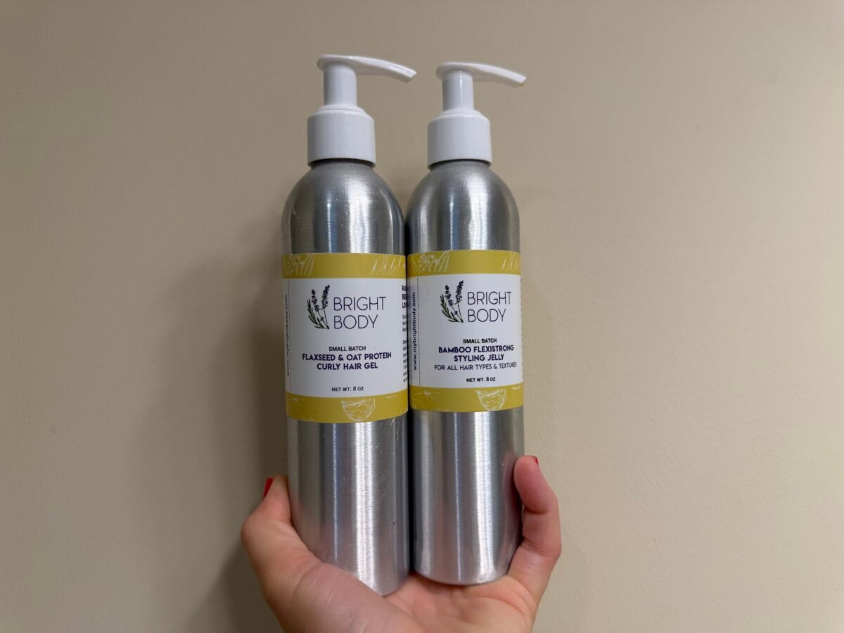 A hand holding two Bright Body hair product bottles, one labeled Flaxseed & Oat Protein Curly Hair Gel and the other Bamboo Flexistrong Styling Jelly.