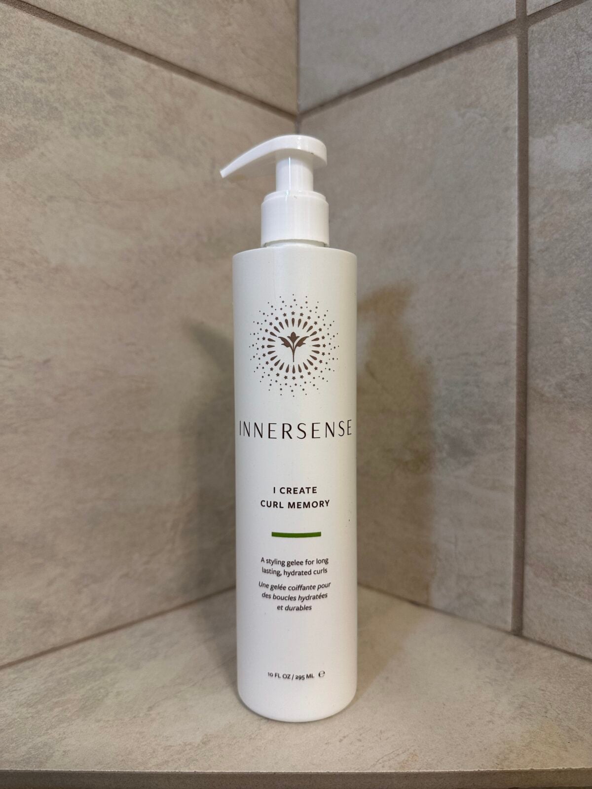 Bottle of Innersense &lsquo;I Create Curl Memory&rsquo; styling gel with a pump top sitting on a tiled shower shelf.