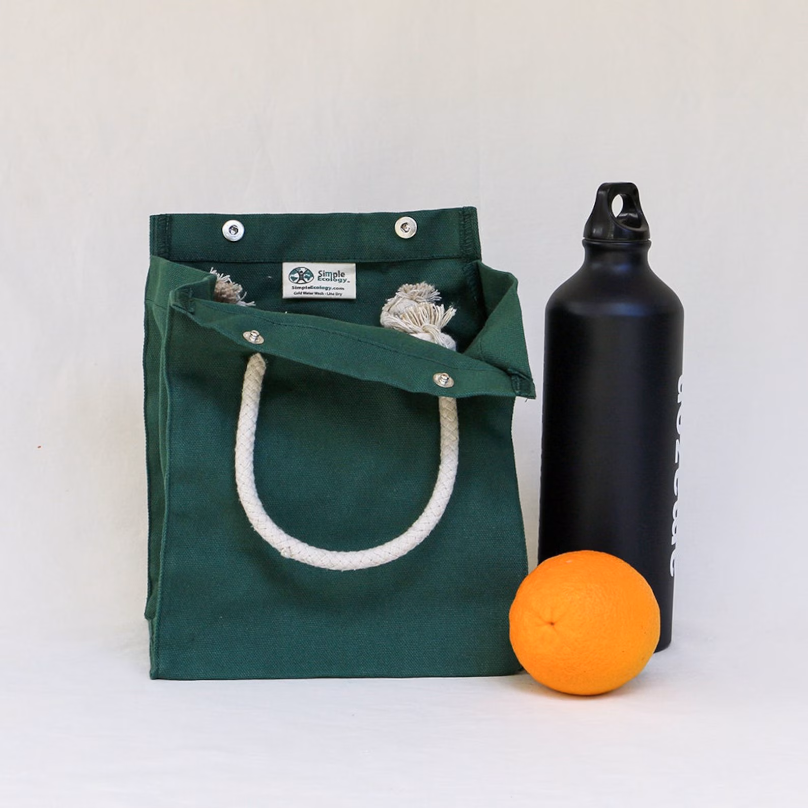 A shot of an Etsy eco-friendly lunch bag, accompanied by a stainless steel tumbler and a fresh orange.