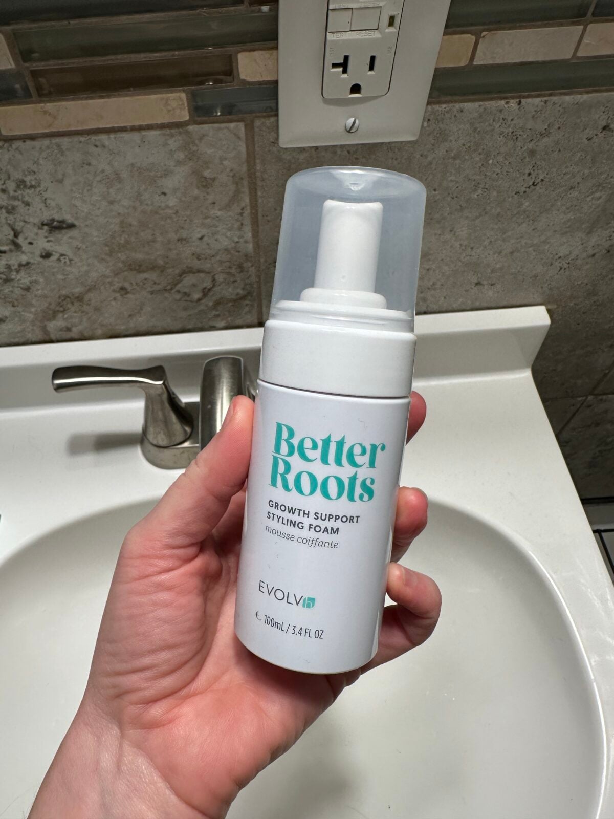 Hand holding EVOLVh Better Roots Growth Support Styling Foam bottle with white and teal packaging and foam pump dispenser