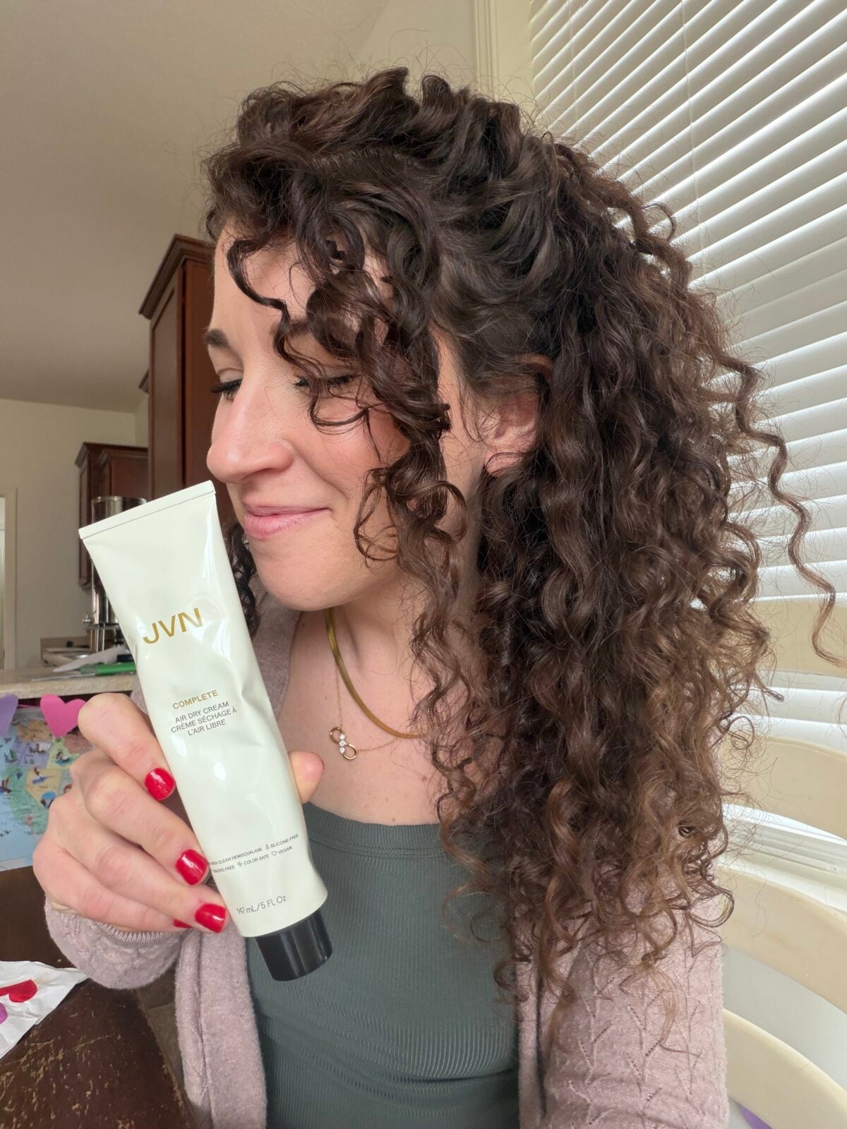A person with curly brown hair holds a tube of JVN Complete Air Dry Cream.