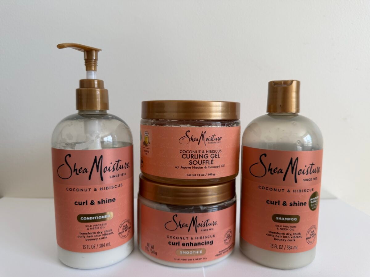 Four SheaMoisture Coconut & Hibiscus hair care products: a pump bottle of conditioner, two stacked jars of curling gel soufflé and curling smoothie, and a bottle of shampoo.