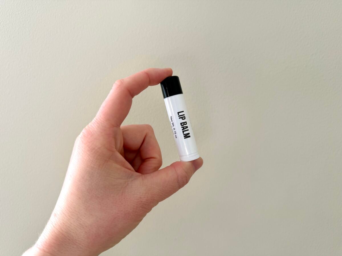 Hand holding Public Goods lip balm tube with black cap against beige wall
