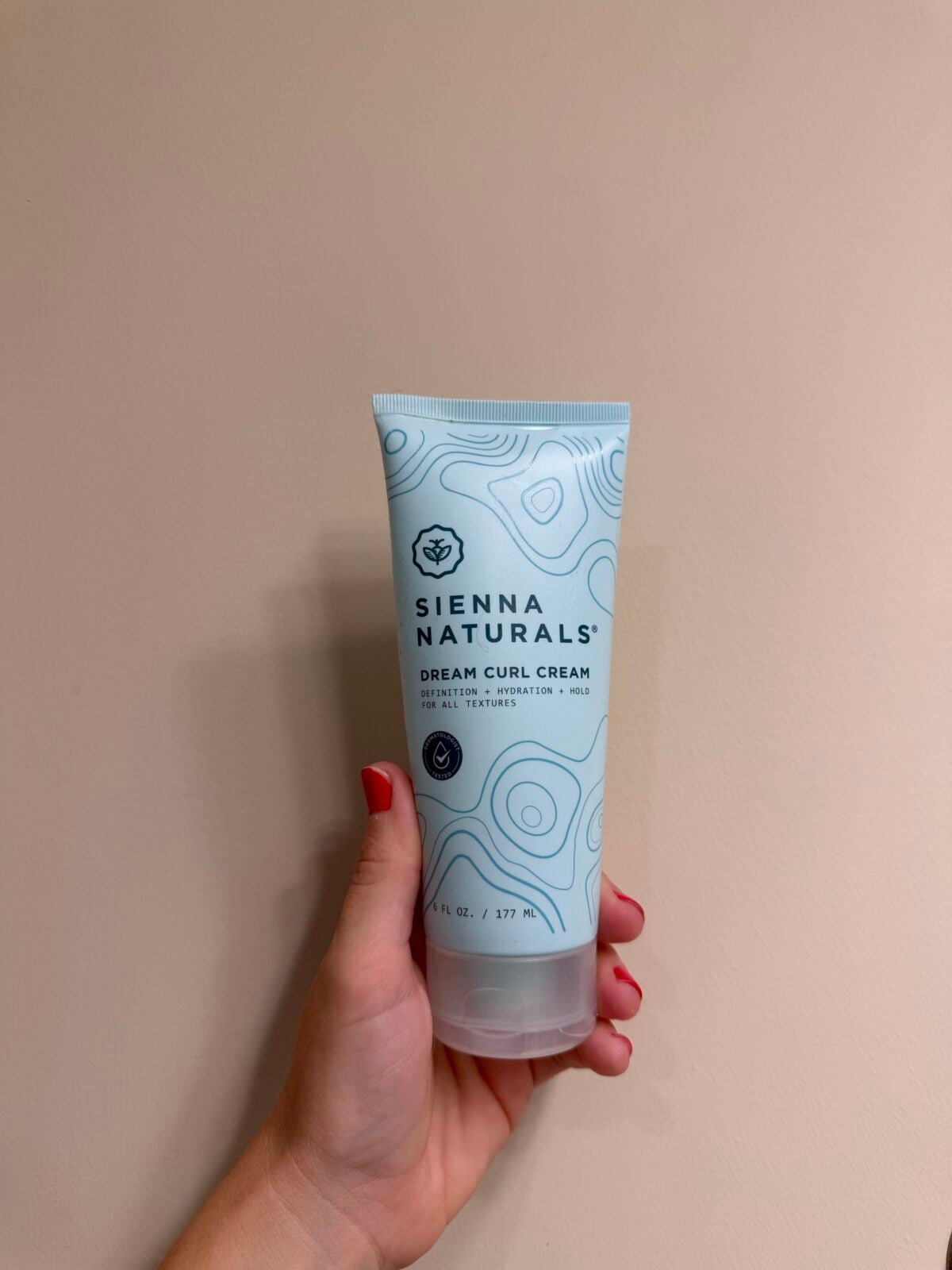 A hand holding a tube of Sienna Naturals Dream Curl Cream.
