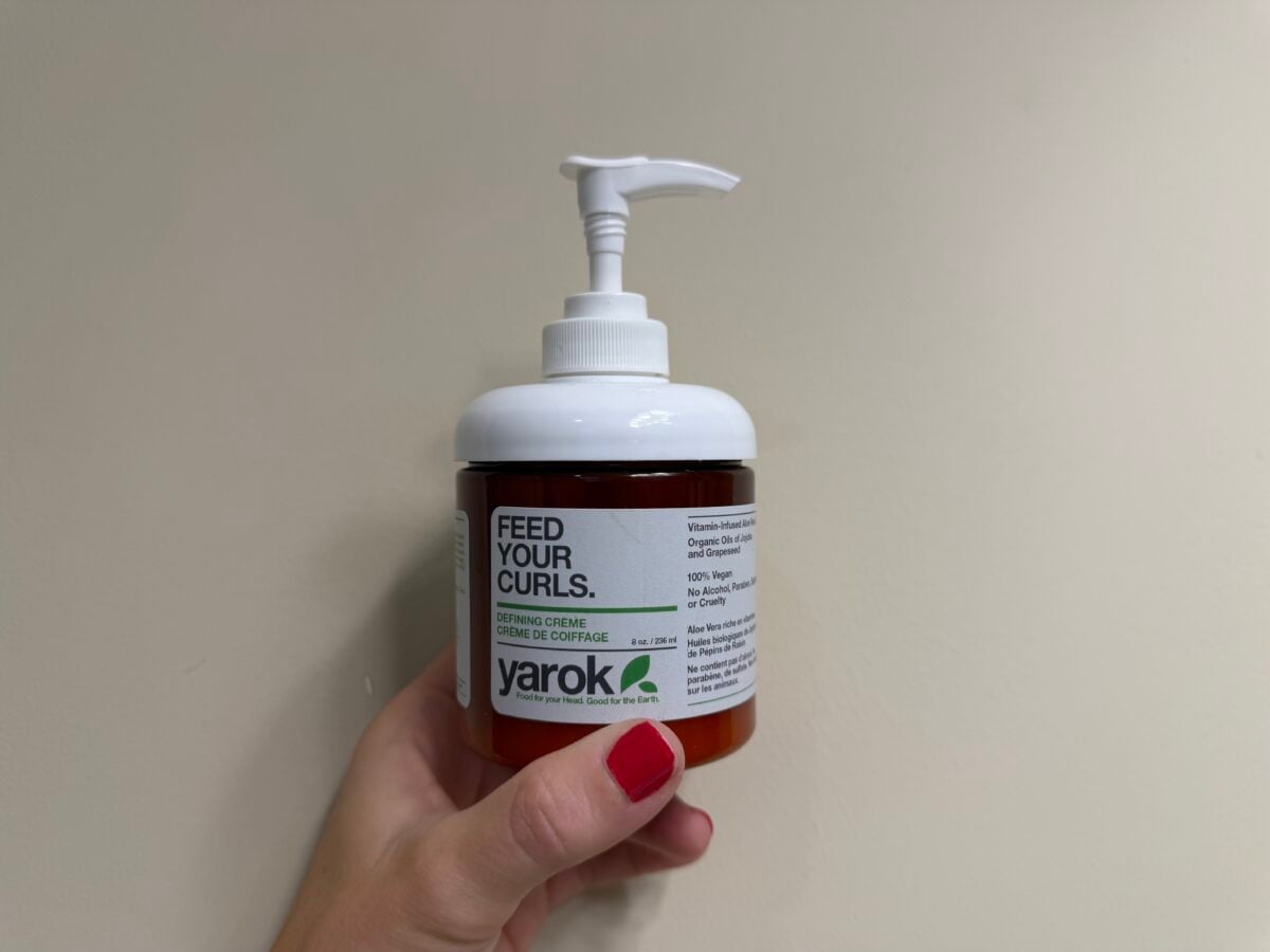 A hand holding a pump bottle of Yarok Feed Your Curls defining creme.