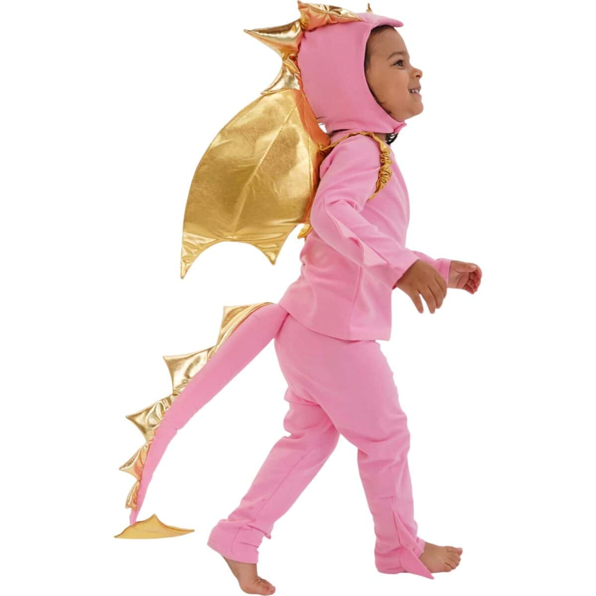 A small child wearing a pink jumpsuit with golden metallic wings and a spiked tail is walking barefoot, looking up and to the side.