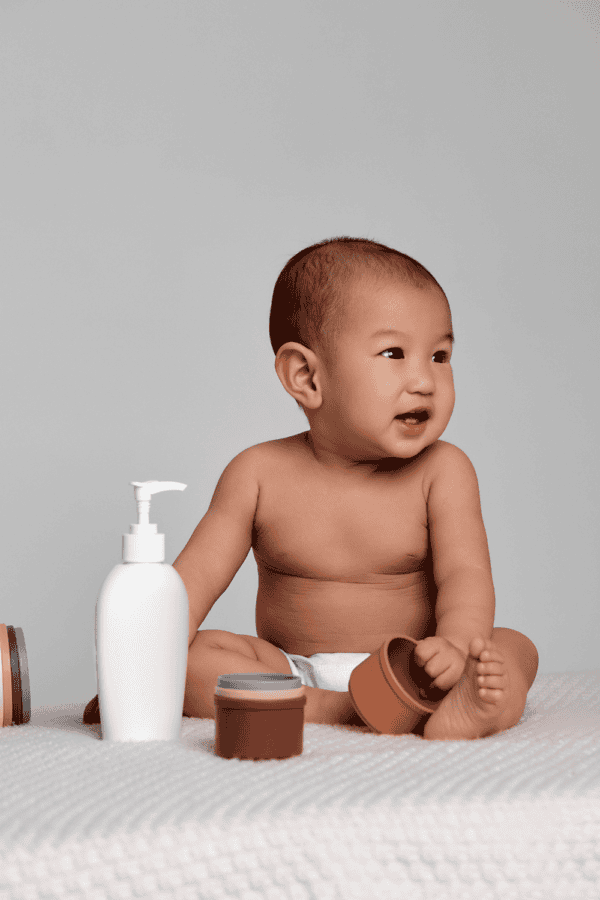 a smiling baby sitting next to a bottle of lotion