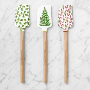Three wooden-handled spatulas with festive holiday designs, including holly, a Christmas tree, and candy canes.