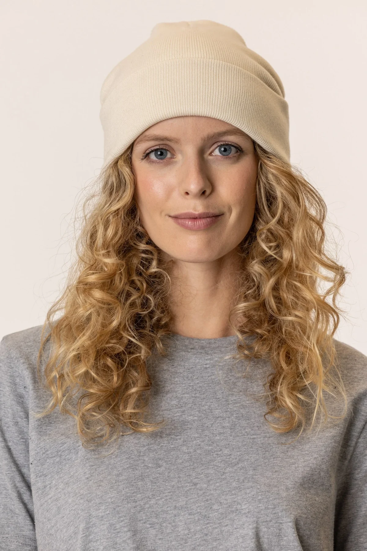 Woman wearing a cream knit beanie and grey top, smiling softly.