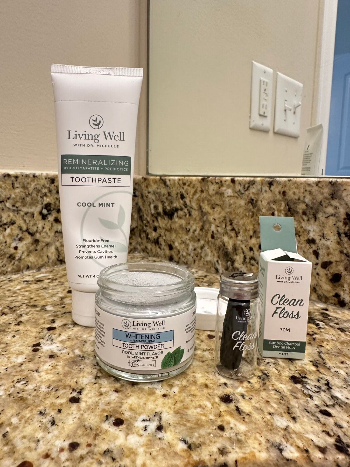 Living Well with Dr. Michelle dental products on a bathroom counter, including remineralizing toothpaste, whitening tooth powder, and bamboo charcoal floss.