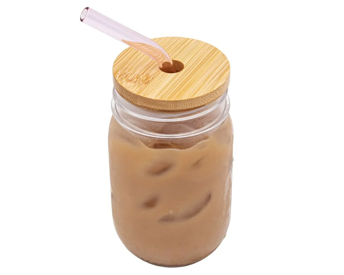 Glass mason jar filled with iced coffee and topped with a bamboo lid, with a pink bent glass straw inserted through the straw hole.