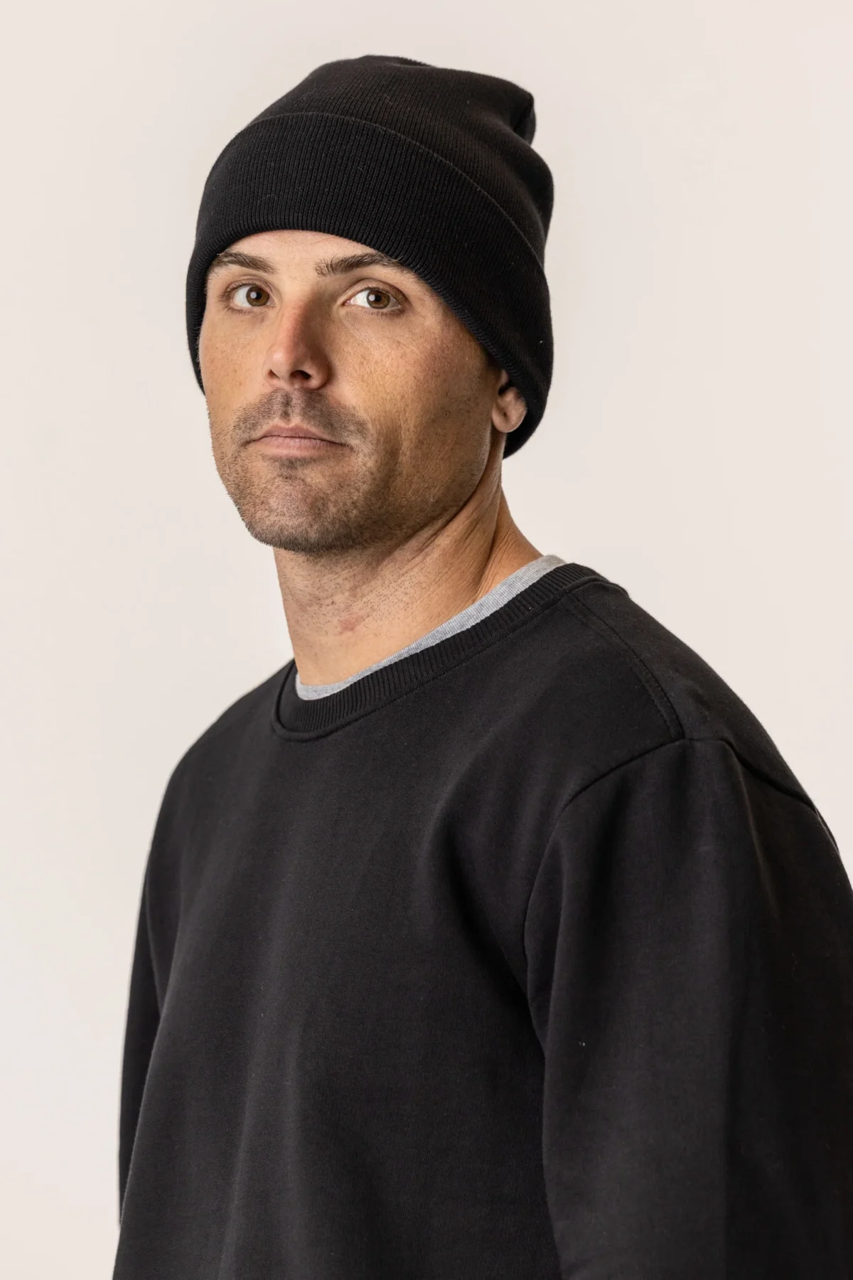 Man wearing a black knit beanie and black sweatshirt, looking toward the camera.