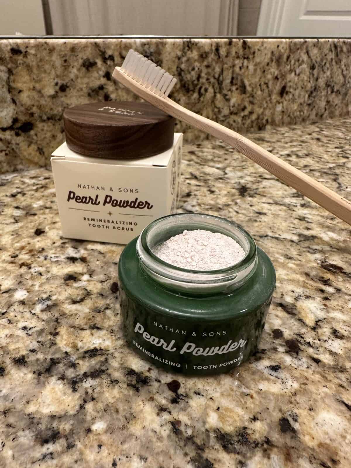 Open jar of Nathan & Sons Pearl Powder tooth scrub on a granite counter with a bamboo toothbrush and product box in the background.
