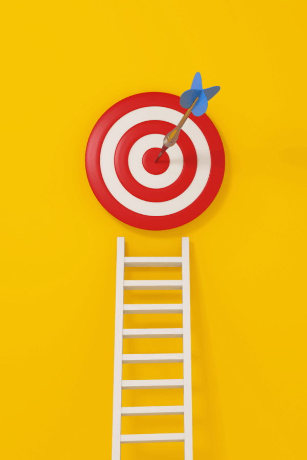 11:53 AMRed and white bullseye target with blue dart in center, white ladder below on yellow background