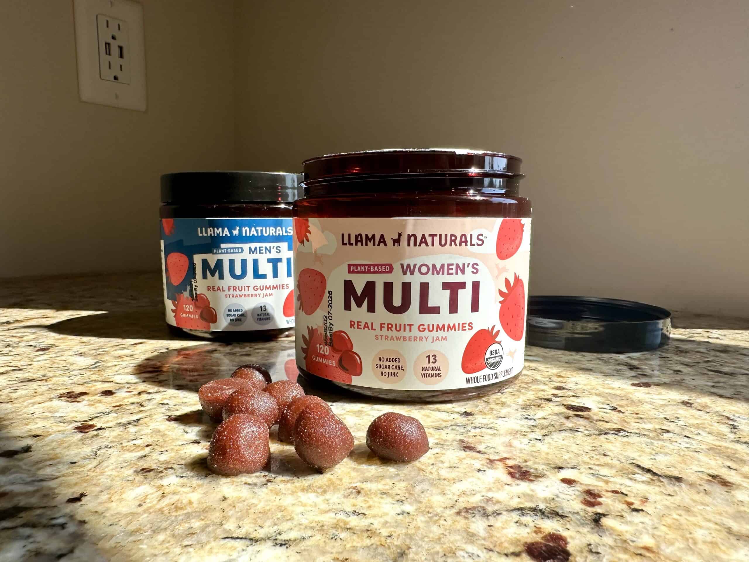 Two containers of Llama Naturals multivitamin gummies, labeled &ldquo;Men&rsquo;s Multi&rdquo; and &ldquo;Women&rsquo;s Multi,&rdquo; sit on a granite counter with several red, sugar-dusted gummies scattered in front.