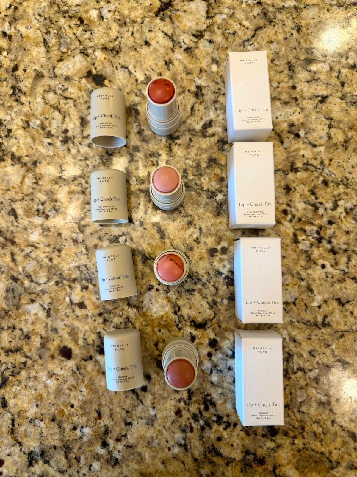 Nine tubes of Merit lip + cheek tint, in three rows of three. Each row shows the product with its box, the open tube, and the closed tube. All items are arranged neatly on a speckled granite countertop.