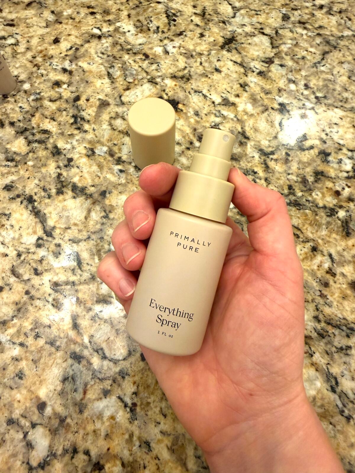 Hand holding Primally Pure Everything Spray bottle on granite countertop