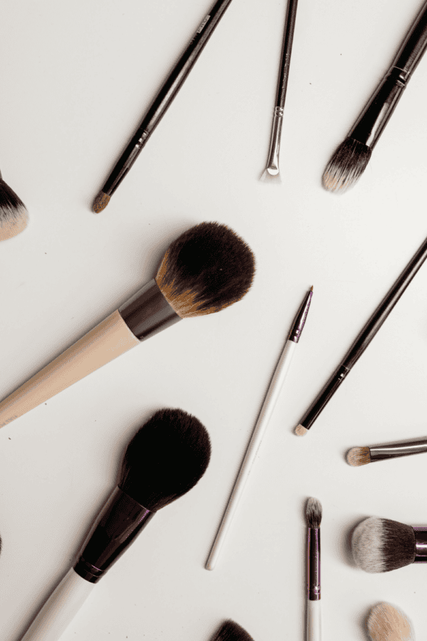 Assorted makeup brushes with black, beige, and white handles, arranged on a white surface, showcasing various shapes and sizes for makeup application.