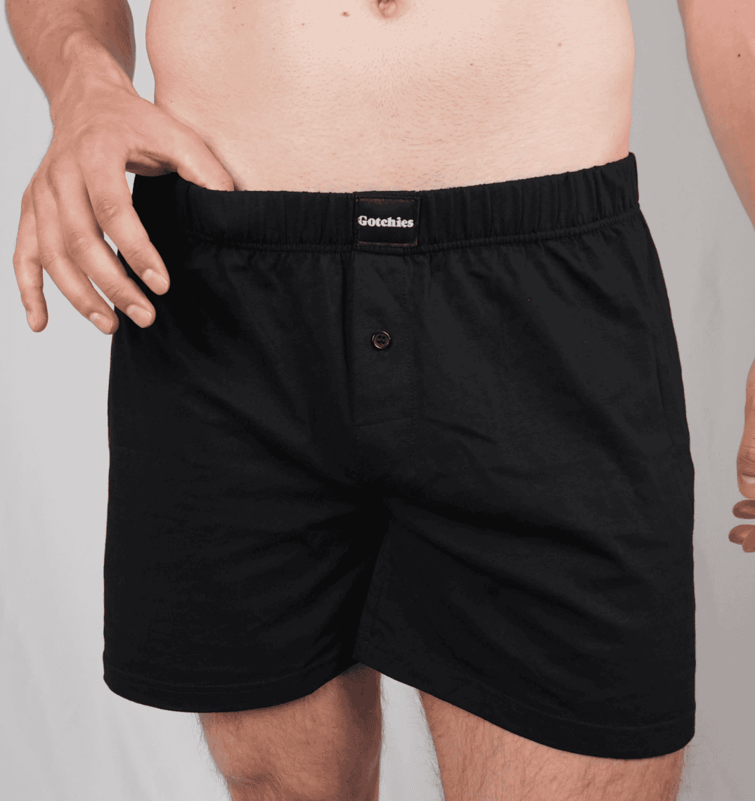 Man wearing black organic cotton boxer shorts from Gotchies, shown from waist to mid-thigh with brand label visible on waistband.