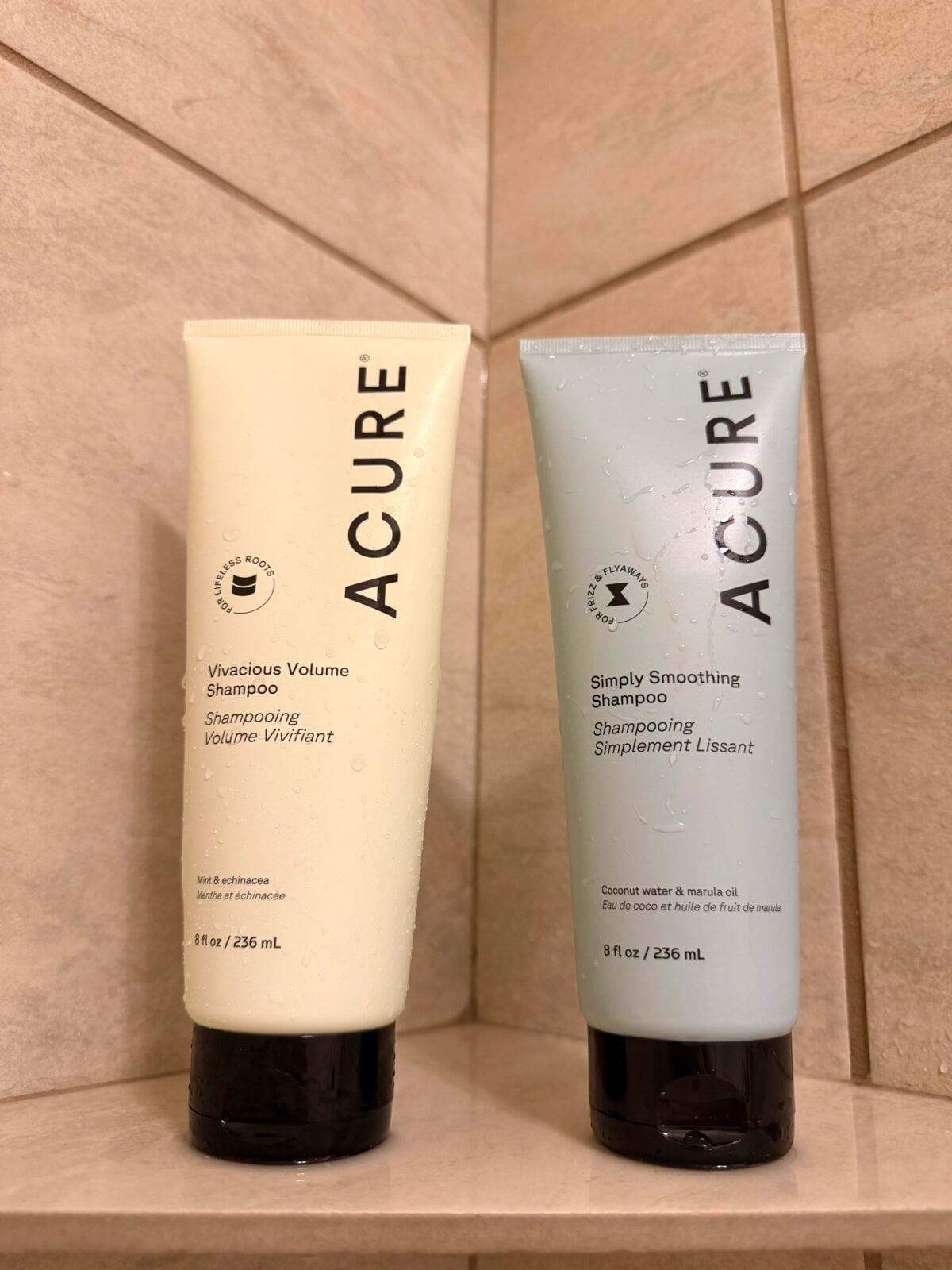 Two bottles of ACURE shampoo are standing side by side on a tiled shower shelf. The left bottle is labeled Vivacious Volume and the right is labeled Simply Smoothing. Both bottles are 8 fl oz / 236 mL.