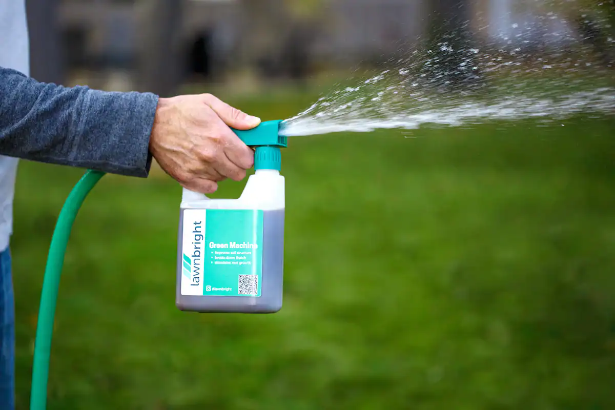Person spraying lawn treatment from a Lawnbright Green Machine bottle attached to a garden hose.