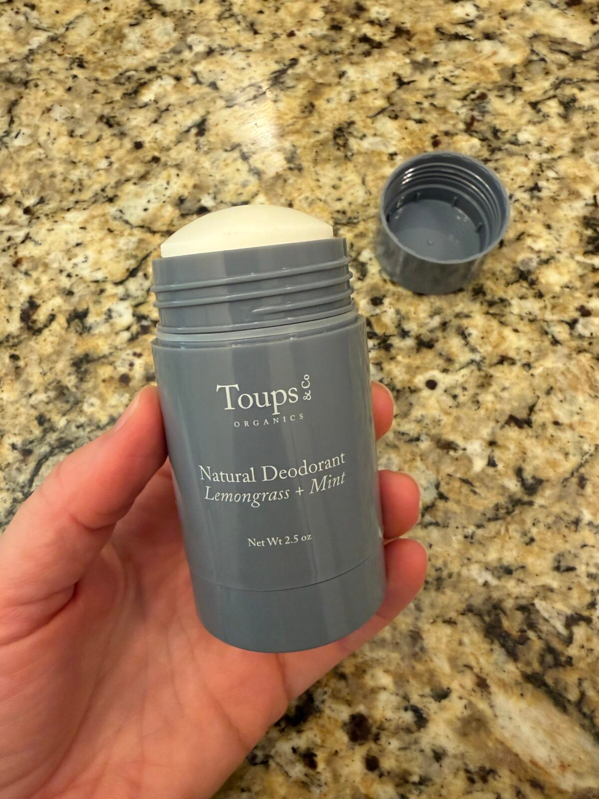 Hand holding Toups & Organics Extra-Strength Natural Deodorant in Lemongrass Mint, 2 oz stick