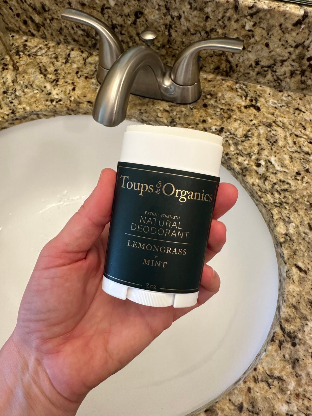 Hand holding Toups & Co Organics Natural Deodorant in Lemongrass + Mint with cap removed showing product