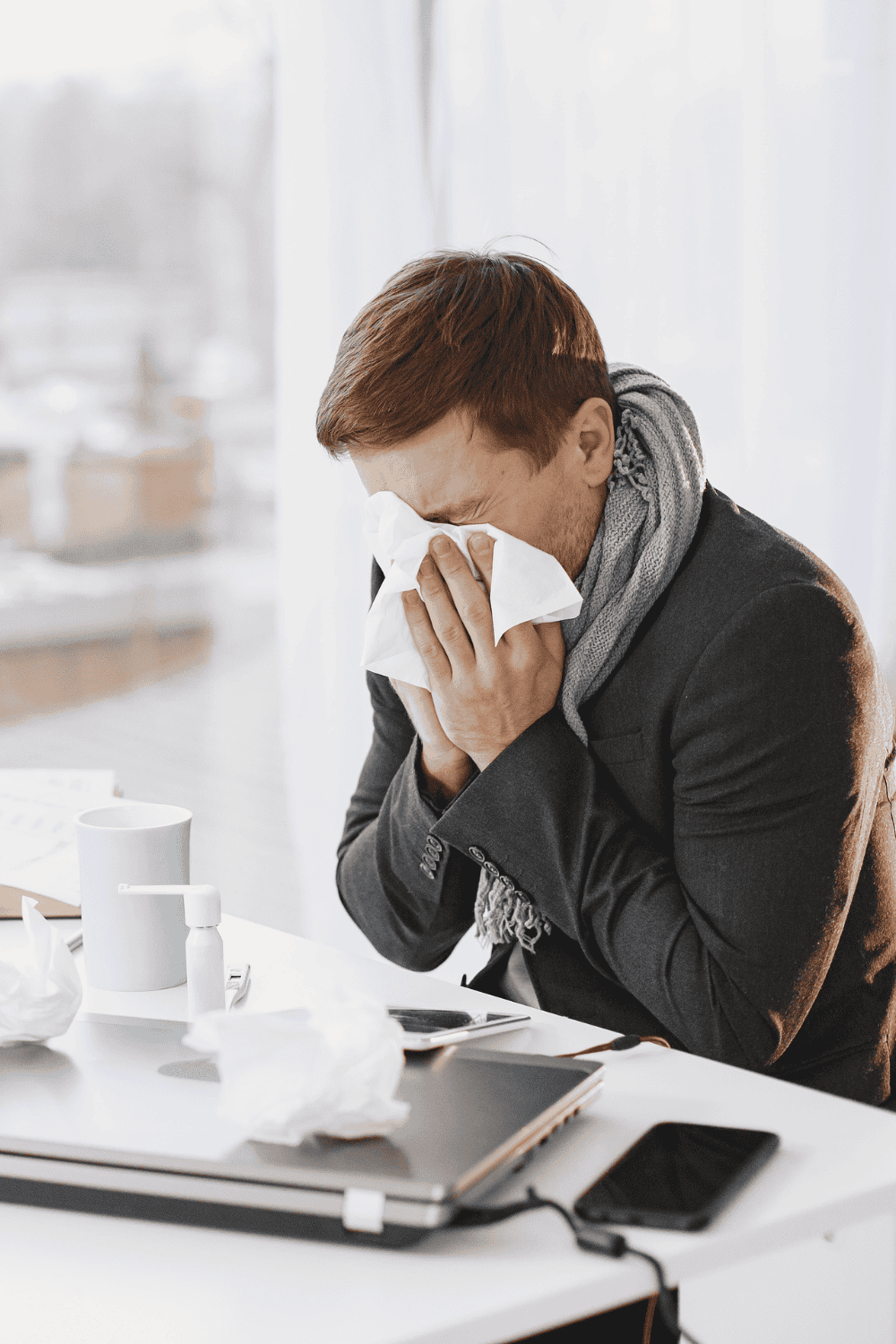 Man in office blowing his nose at desk, surrounded by tissues