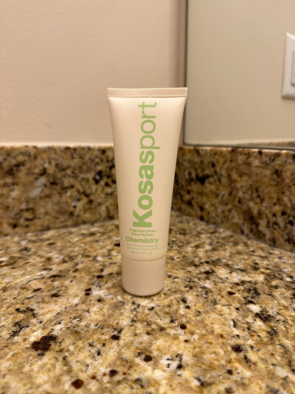 A Kosasport Chemistry fragrance-free deodorant tube standing upright on a granite bathroom countertop near a mirror.