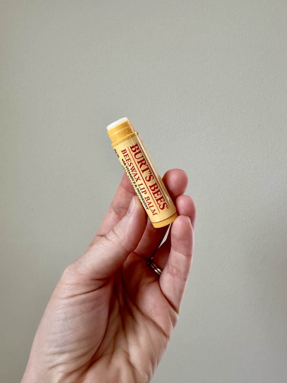 Hand holding a Burt’s Bees Beeswax Lip Balm tube against a plain background.