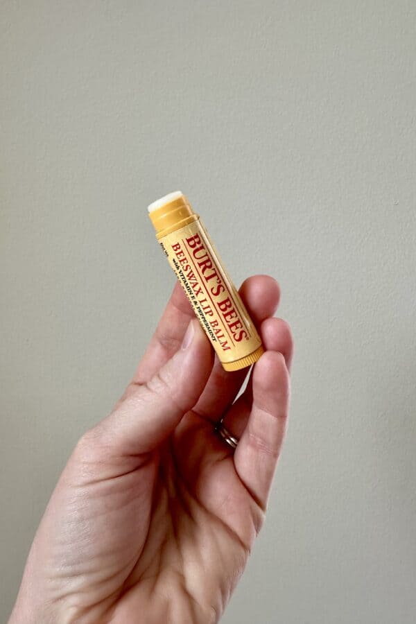 Hand holding a Burt’s Bees Beeswax Lip Balm tube against a plain background.