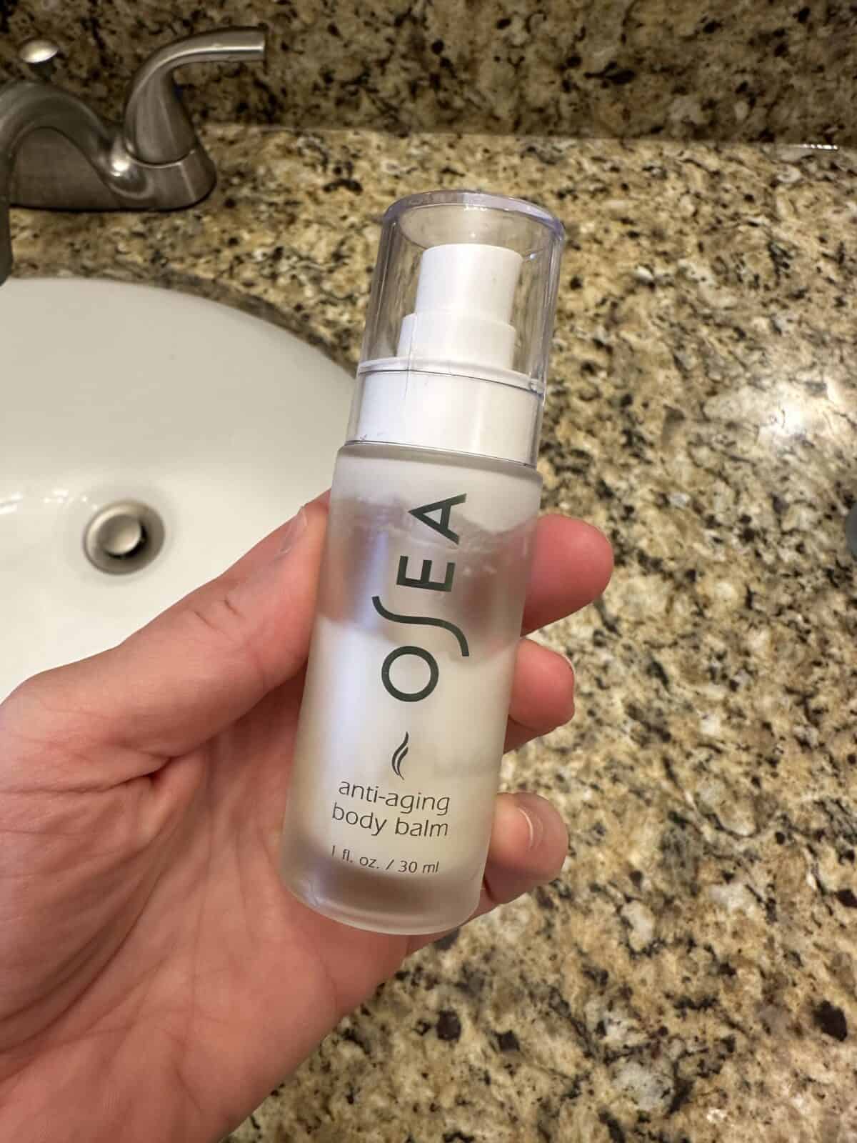 A person holding the OSEA Anti-Aging Body Balm near the sink in the bathroom