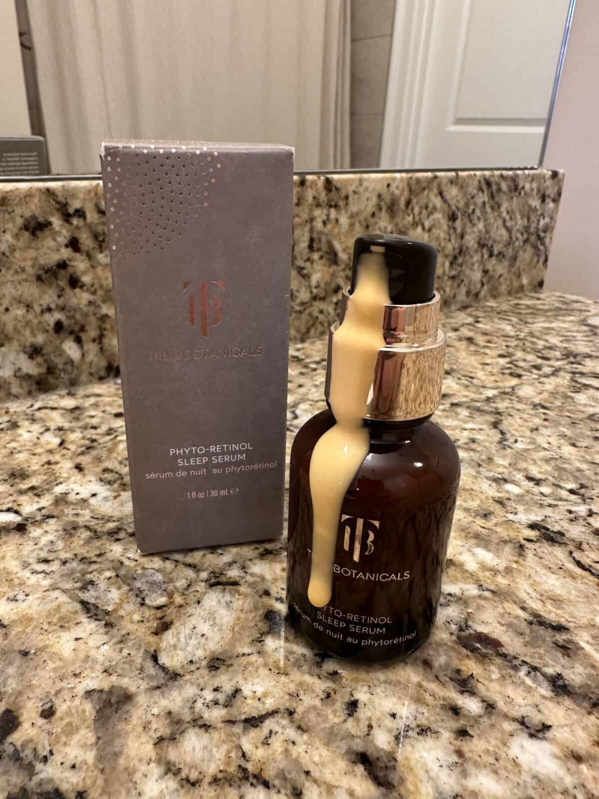 The photo shows the Phyto-Retinol Sleep Serum from True Botanicals with its box arranged on a granite countertop with a bathroom mirror in the background.