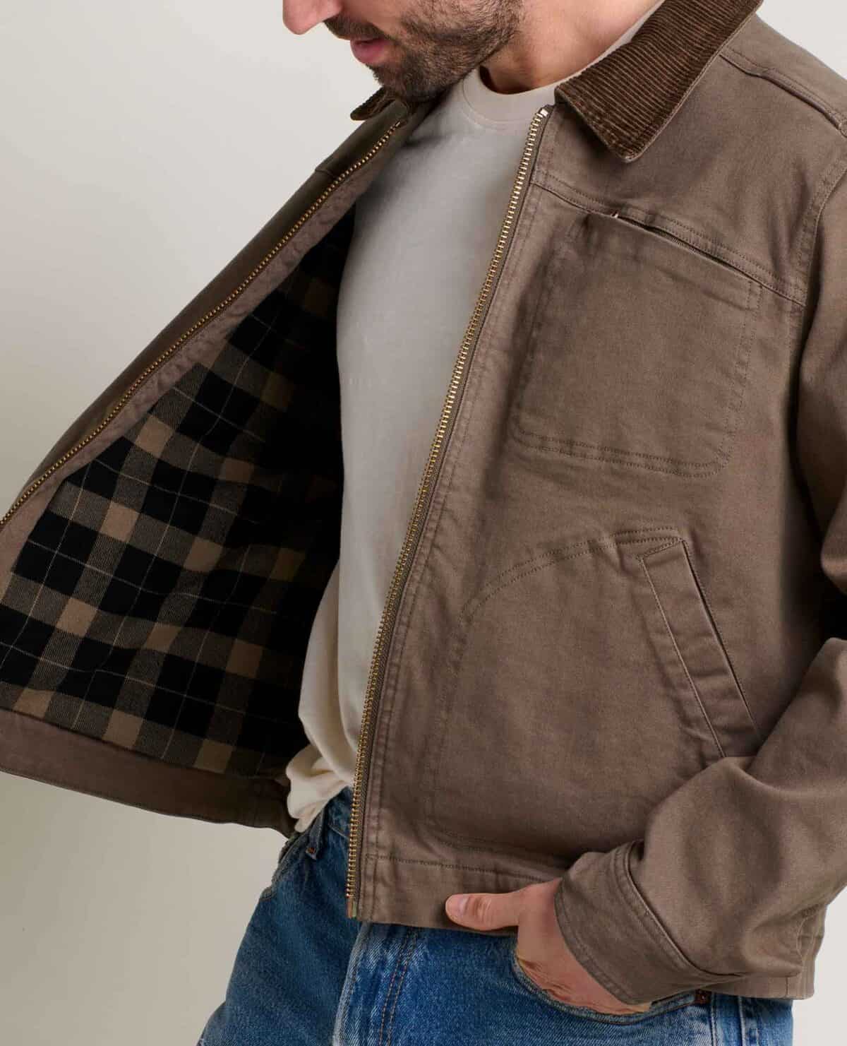 A close-up, cropped shot shows a man wearing a brown, zip-up jacket from Toad & Co. with a plaid lining, a corduroy collar, and a light-colored t-shirt underneath.