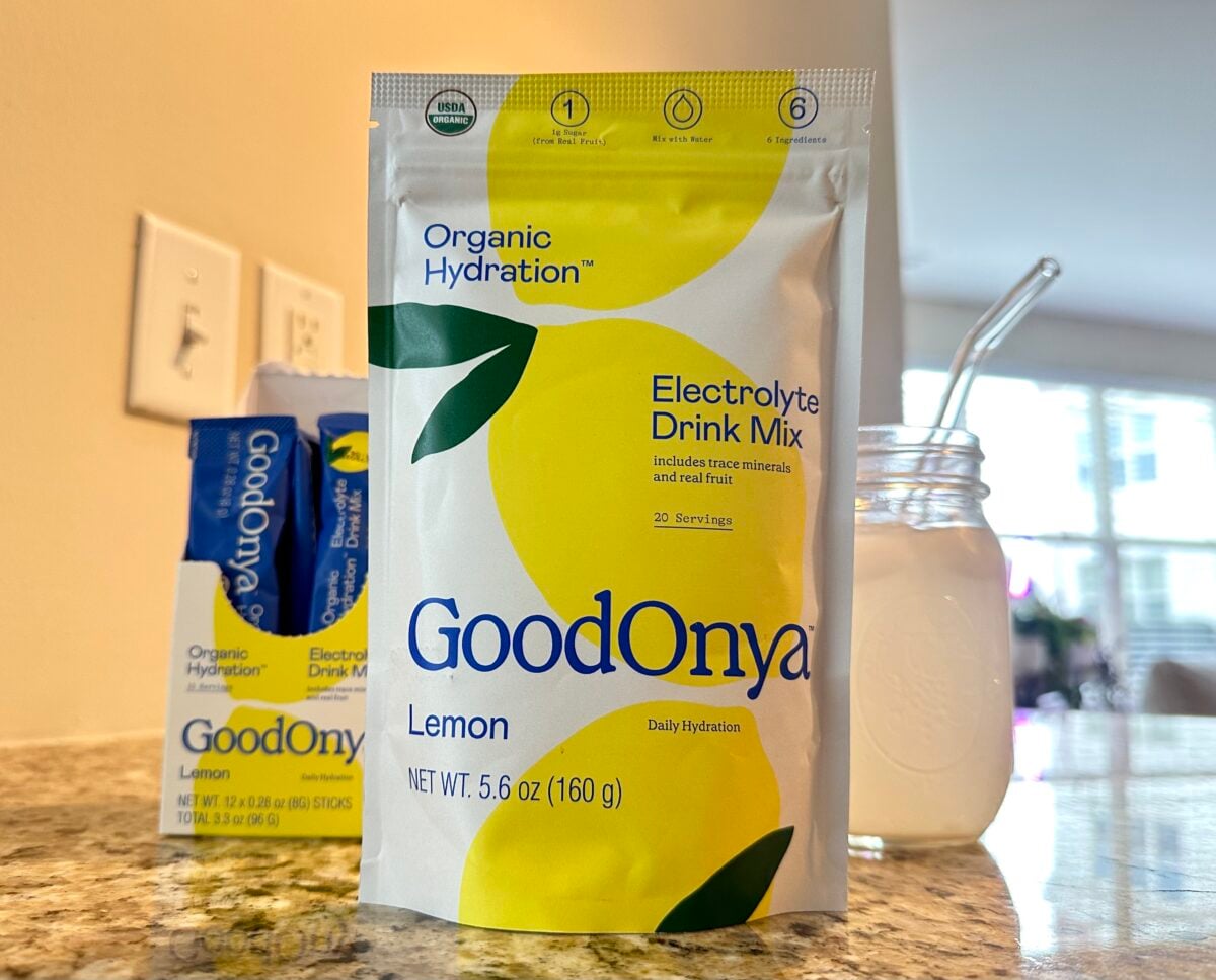 The photo features a large yellow and white pouch of Goodonya Organic Hydration Lemon Electrolyte Drink Mix next to a glass of the prepared drink, with a small box of individual packets visible in the background.