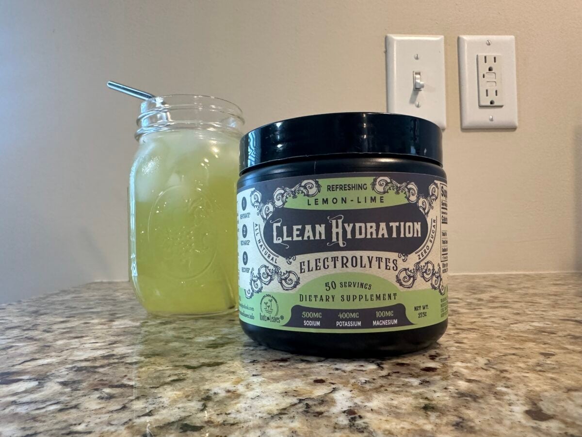 The photo shows a bottle of black-bottled "Clean Hydration Electrolytes" in Lemon-Lime flavor next to a mason jar filled with a matching yellow-green iced drink, both resting on a speckled countertop near a white light switch and outlet plate.