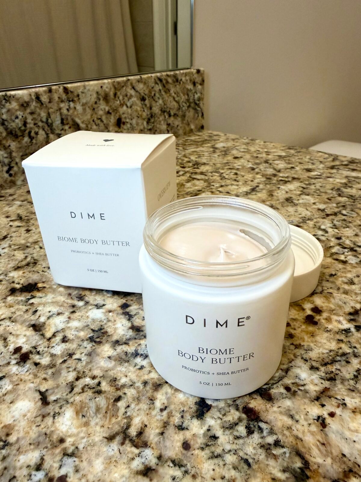 Open jar of DIME Biome Body Butter on a granite bathroom counter, with the product box behind it.
